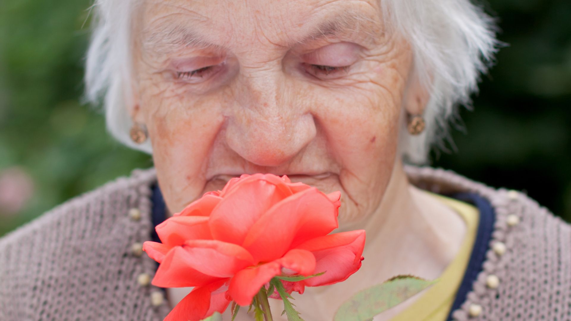 Mujer mayor oliendo una rosa