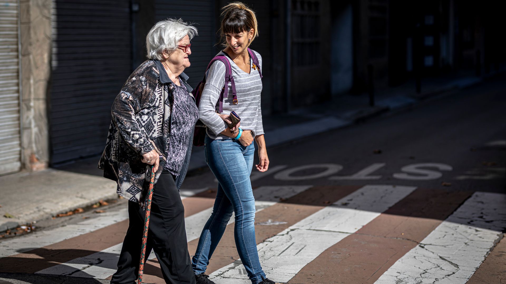 Profesional de Suara acompanyando a una mujer mayor dependiente a cruzar la calle