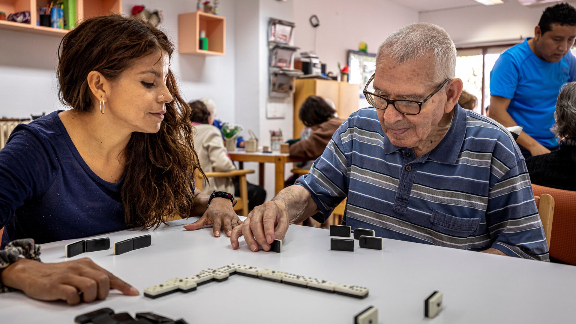 Persona mayor jugando al domino con una profesional en el centro de día