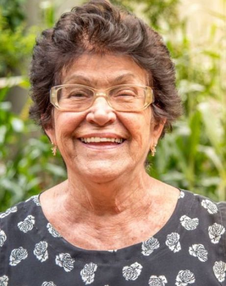 Mujer con alzheimer mirando a cámara sonriente delante de un fondo verde naturaleza
