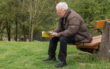 Hombre mayor sentado en un banco leyendo un libro con instrucciones