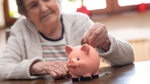 Mujer mayor poniendo monedas dentro de una hucha en forma de cerdito