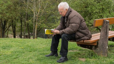 Hombre mayor sentado en un banco leyendo un libro con instrucciones