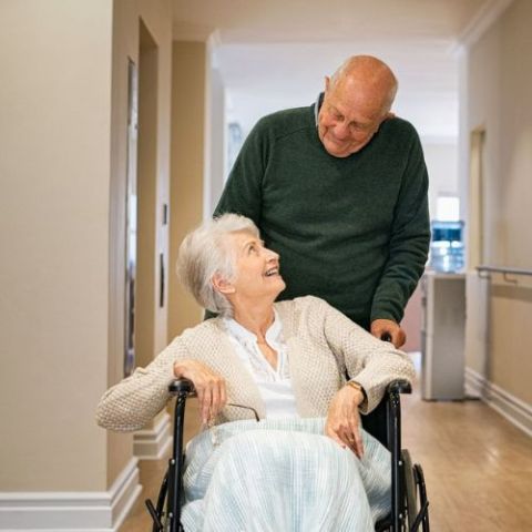 Persona acompañando a una persona atendida con silla de ruedas en una residencia 