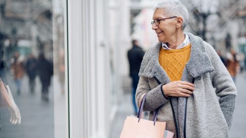 Mujer mayor andando por la calle mirando escaparates yendo de compras