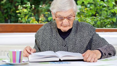 Mujer mayor leyendo un libro y tomando un té